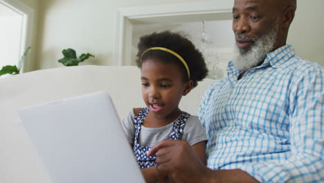 Glücklicher-Afroamerikanischer-Großvater-Mit-Enkelin,-Die-Im-Wohnzimmer-Ein-Tablet-Benutzt