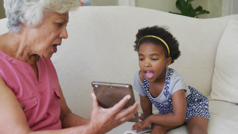 Feliz-Abuela-Afroamericana-Con-Nieta-Usando-Tableta-En-La-Sala-De-Estar