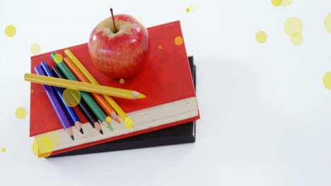 Animation-of-yellow-spots-over-apple-and-colour-pencils-on-stack-of-books