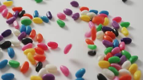 Video-of-close-up-of-multi-coloured-sweets-falling-over-white-background