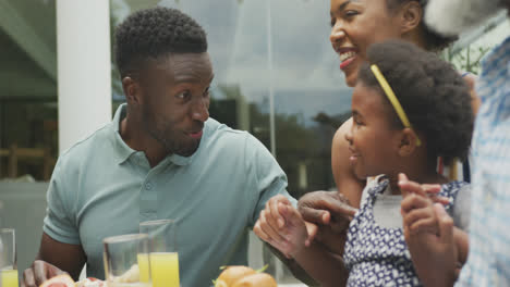 Happy-african-american-family-talking-and-having-breakfast-in-garden