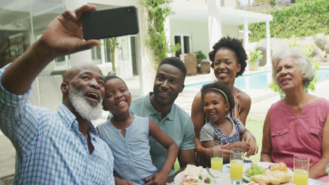 Happy-african-american-family-taking-selfie-and-having-breakfast-in-garden