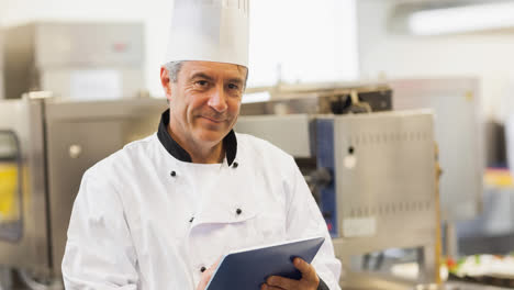 Un-Chef-Masculino-Caucásico-Sonriente-Con-Delantal-Usando-Una-Tableta-En-Una-Cocina-Profesional