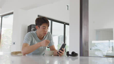 Asiatischer-Junge-Benutzt-Smartphone-Beim-Frühstück-Im-Wohnzimmer-Zu-Hause