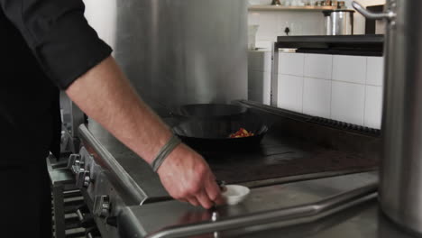 Caucasian-male-chef-frying-vegetables-in-frying-pan-with-bursting-fire-in-kitchen,-slow-motion