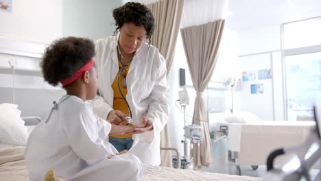 African-american-female-doctor-examining-girl-using-stethoscope-in-hospital-room,-slow-motion