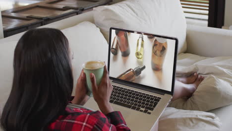Biracial-woman-using-laptop-on-couch-at-home-online-shopping-for-beauty-products,-slow-motion