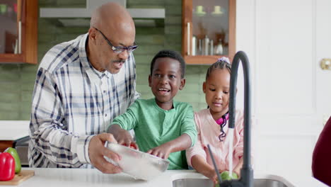 Happy-african-american-grandparents-and-grandchildren-washing-vegetables-in-kitchen,-slow-motion
