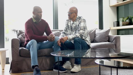 Happy-african-american-senior-father-and-son-sitting-on-couch,talking-and-shaking-hands,-slow-motion