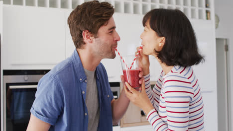 Video-of-happy-diverse-couple-drinking-juice-with-straws-in-kitchen