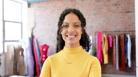 Portrait-of-biracial-female-fashion-designer-with-dark-curly-hair-smiling-in-studio,-slow-motion