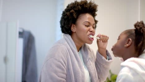 Young-African-American-mother-brushes-her-teeth-at-home,-with-daughter