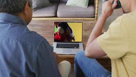Biracial-father-and-son-watching-laptop-with-diverse-male-rugby-players-playing-on-screen