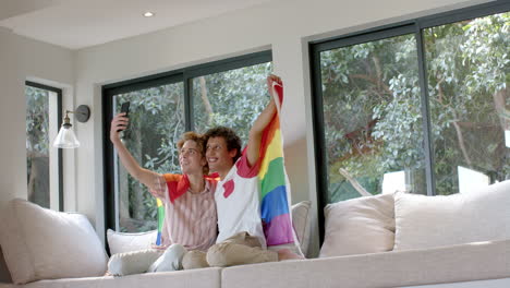 Diverse-gay-male-couple-with-rainbow-lgbt-flag,-using-smartphone-at-home,-slow-motion,-copy-space
