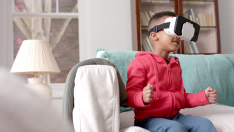 African-american-boy-using-vr-headset-and-touching-virtual-screen-in-living-room,-slow-motion