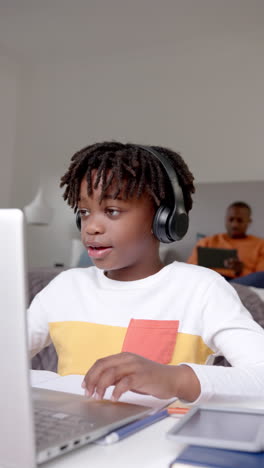 Vertical-video-of-african-american-boy-using-laptop-for-online-lesson-at-home,-slow-motion