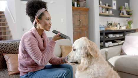 Happy-biracial-woman-petting-dog-and-talking-on-smartphone-at-home,-slow-motion