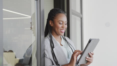 Portrait-of-happy-african-american-casual-businesswoman-using-tablet-in-office-doorway,-slow-motion