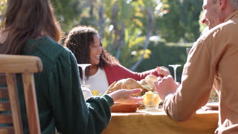 Happy-diverse-male-and-female-friends-saying-prayer-on-thanksgiving-celebration-meal-in-sunny-garden