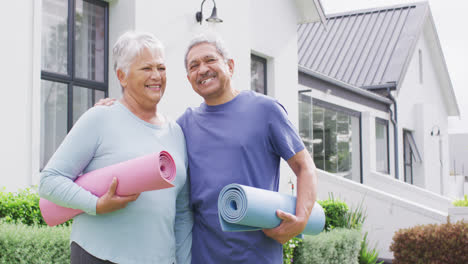 Portrait-of-happy-senior-diverse-couple-with-yoga-mats-in-garden