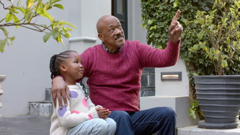 Glücklicher-Afroamerikanischer-Großvater-Und-Enkelin-Sitzen-Und-Reden-Im-Garten,-Zeitlupe