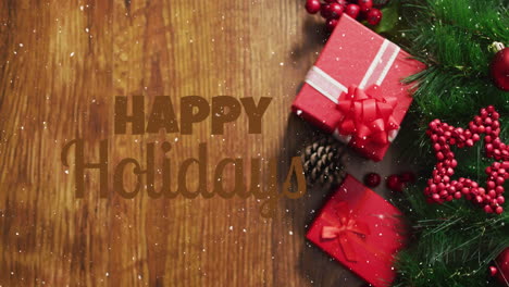 Animation-of-snow-falling-over-happy-holidays-text-against-gifts-and-decorations-on-wooden-surface