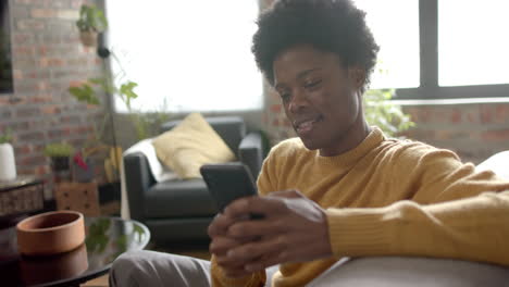 Happy-african-american-man-sitting-on-sofa-using-smartphone-at-home,-slow-motion
