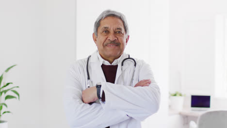 Video-portrait-of-biracial-male-doctor-standing-with-arms-crossed-smiling-to-camera