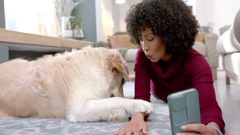 Happy-biracial-woman-with-golden-retriever-dog-using-smartphone-at-home,-slow-motion