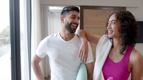 Portrait-of-happy-biracial-couple-holding-yoga-mats-at-home,-in-slow-motion