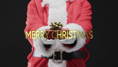 Merry-christmas-text-in-gold-over-midsection-of-santa-holding-present-on-black-background