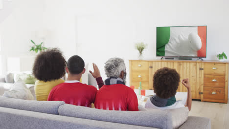 Biracial-family-watching-tv-with-rugby-ball-on-flag-of-ivory-coast-on-screen