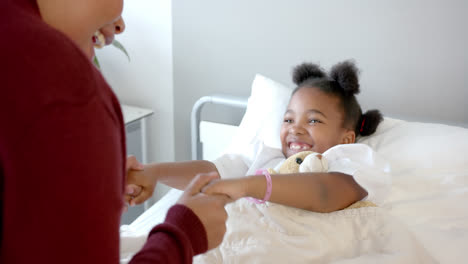 Happy-african-american-mother-fooling-with-daughter-lying-in-hospital-bed-with-mascot,-slow-motion