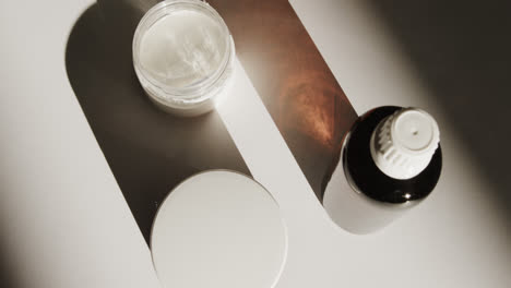 High-angle-view-of-glass-bottle-and-cream-tubs-with-copy-space-on-white-background