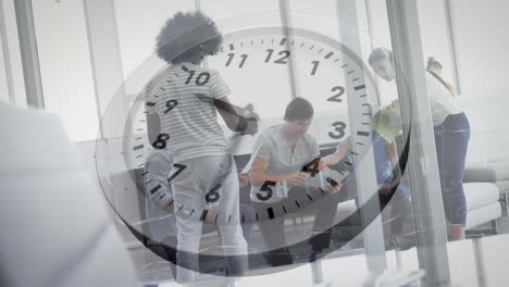 Animation-of-ticking-clock-against-team-of-diverse-colleagues-discussing-together-at-office