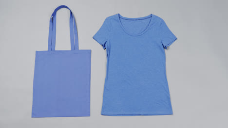 Primer-Plano-De-Bolsa-Azul-Y-Camiseta-Sobre-Fondo-Gris,-Con-Espacio-Para-Copiar,-Cámara-Lenta