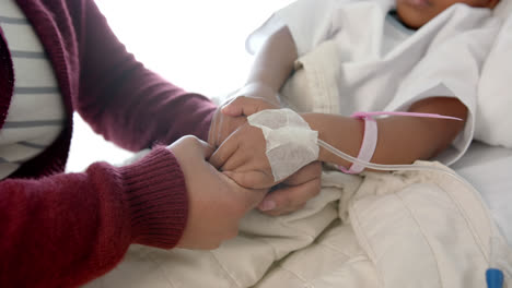 Holding-hands-of-african-american-mother-and-daughter-lying-in-hospital-bed,-slow-motion