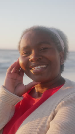 Vertikales-Video-Eines-Porträts-Einer-Glücklichen-älteren-Afroamerikanischen-Frau,-Die-Am-Strand-Lächelt,-In-Zeitlupe