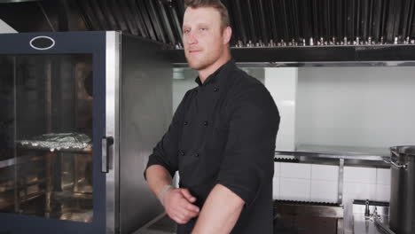 Portrait-of-happy-caucasian-male-chef-in-black-smiling-in-kitchen,-slow-motion