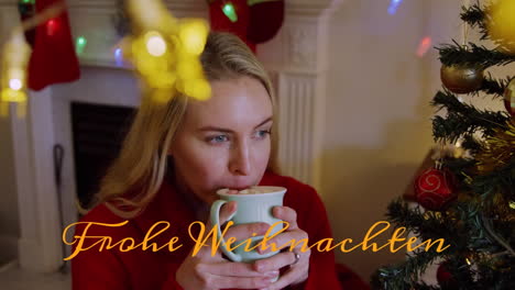 Animation-of-frohe-weihnachten-text-banner-against-caucasian-woman-drinking-hot-chocolate-at-home