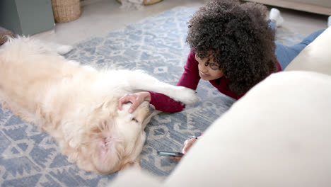Happy-biracial-woman-with-golden-retriever-dog-using-smartphone-at-home,-slow-motion