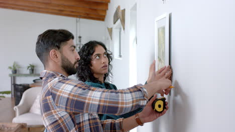 Happy-biracial-couple-taking-measurements-on-wall-at-home,-in-slow-motion