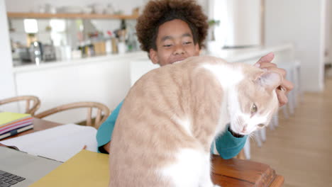 Happy-african-american-boy-sitting-at-table,-petting-his-pet-cat,-slow-motion