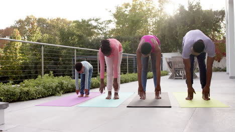 Happy-african-american-parents,-son-and-daughter-practicing-yoga-in-sunny-garden,-in-slow-motion