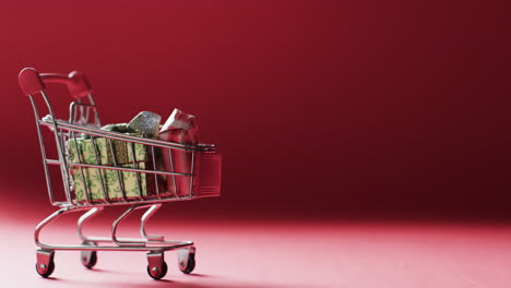Video-of-shopping-trolley-with-christmas-gifts-and-copy-space-on-red-background