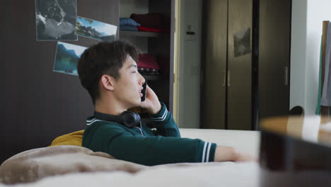 Asiatischer-Junge,-Der-Zu-Hause-Auf-Der-Couch-Sitzt-Und-Auf-Dem-Smartphone-Spricht
