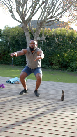 Vertical-video-of-african-american-man-fitness-training-exercising-on-deck-in-garden,-slow-motion
