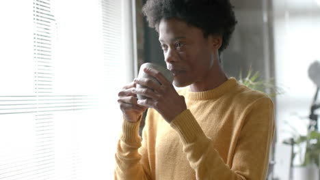 Nachdenklicher-Afroamerikanischer-Mann,-Der-Kaffee-Trinkt-Und-Zu-Hause-Durch-Das-Fenster-Schaut,-Zeitlupe