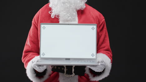 Video-Vom-Weihnachtsmann,-Der-Einen-Laptop-Mit-Kopierplatz-Auf-Schwarzem-Hintergrund-Hält