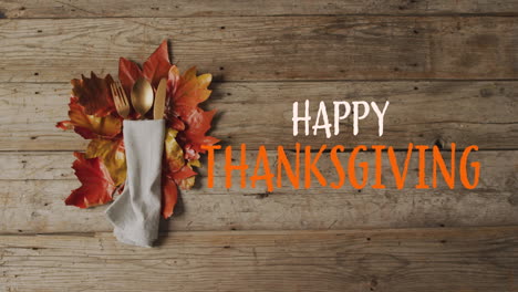 Animation-of-happy-thanksgiving-text-over-cutlery-and-autumn-leaves-over-wooden-surface